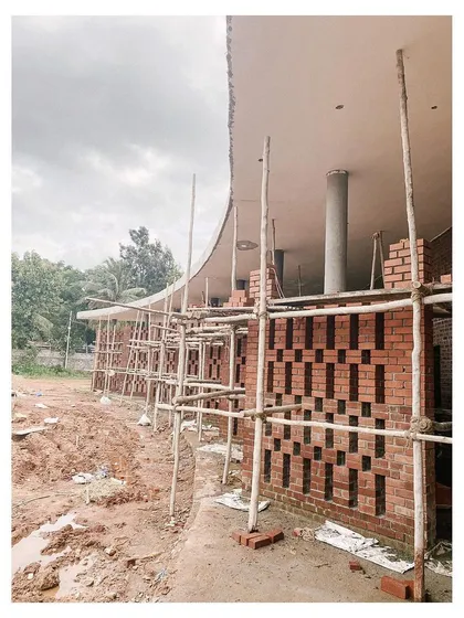 A construction site view of the curved brick wall, showing the raw, muddy ground that will later become a landscaped garden.