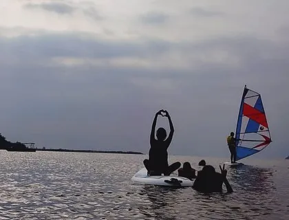 The silhouette of campers enjoying a paddleboard and windsurfer against the evening sky in Karwar.