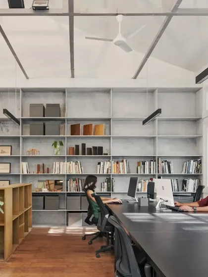 Large windows, a double-height pitched ceiling, and warm wooden floors create an open and inspiring workspace. The open display of books, samples, and models makes it a true design studio.