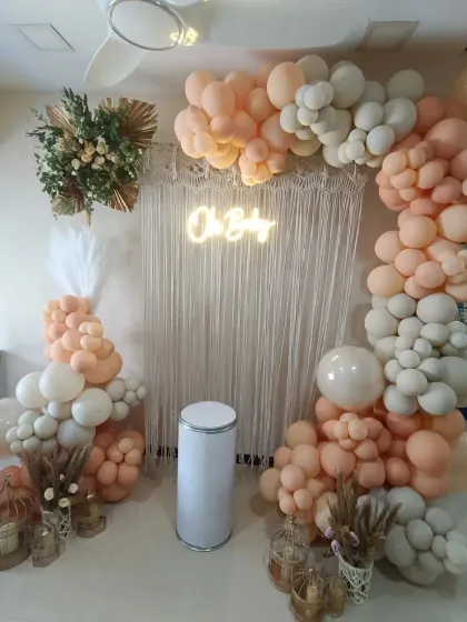 This is a trendy boho baby shower design, using a neutral color palette of peach and cream balloons. The macrame backdrop, dried pampas grass, and a warm 'Oh Baby' neon sign create a chic and relaxed vibe for your celebration.