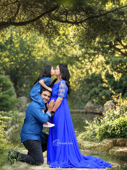 A precious family portrait in a beautiful garden. The older daughter, perched on her dad's shoulders, gives her mom a kiss.