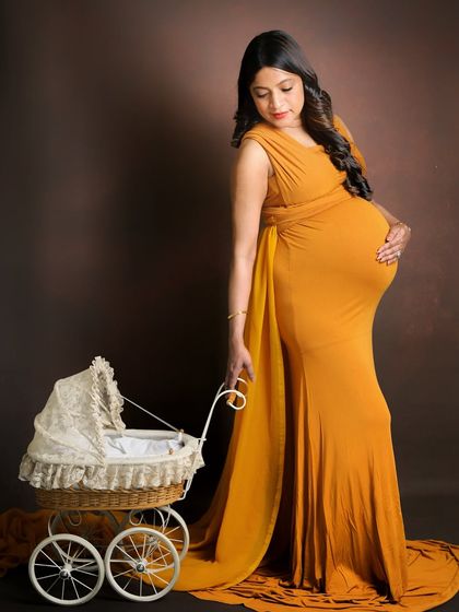 A gentle and classic portrait using a vintage-style pram as a prop. The mom-to-be looks down lovingly in her elegant mustard gown, creating a timeless and tender image.