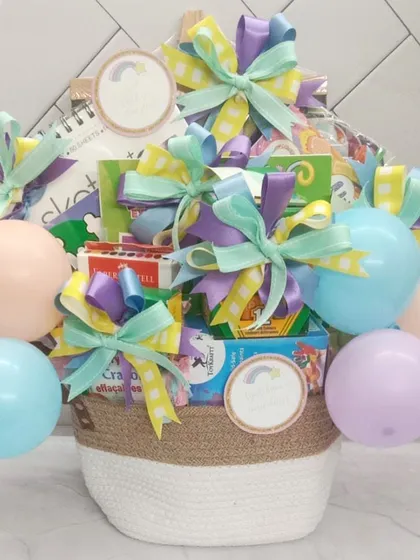 A custom art supplies gift basket for a creative star. This pastel-themed basket is filled with sketchbooks, crayons, and other art materials, topped with a balloon bouquet.