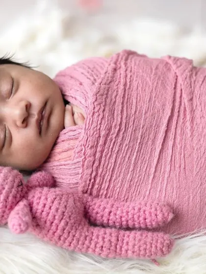 Sleeping soundly in a miniature bed, this newborn is surrounded by soft pink flowers. These styled setups create beautiful, dreamy portraits.