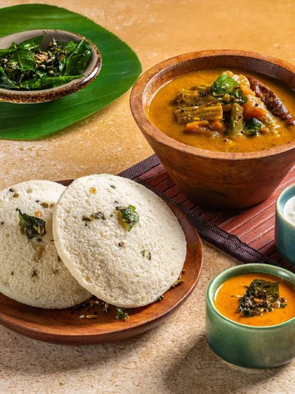 A close-up of steamed idlis served on a banana leaf, emphasizing their soft, fluffy texture for Gulab Sweets.