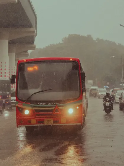 A red bus with its headlights on cuts through the heavy rain. This shot captures the motion and atmosphere of commuting in Mumbai during a downpour.