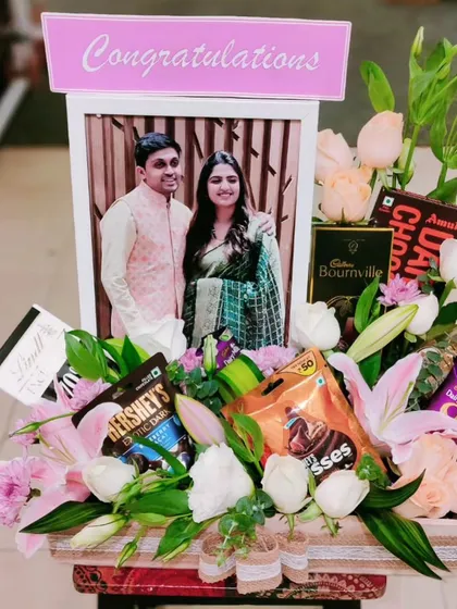 Congratulate a happy couple with this stunning floral hamper. A personalized photo frame is surrounded by a beautiful bouquet of pink lilies, roses, and various chocolates.