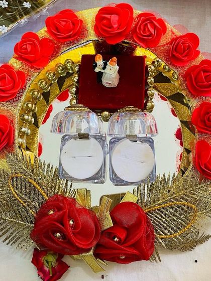 A beautifully decorated aarathi plate for an engagement ring ceremony. It includes small containers for the rings, surrounded by red roses and golden accents.