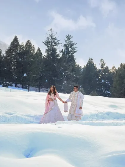 A romantic destination pre-wedding photo of a couple walking hand-in-hand through a vast, snowy landscape, capturing the scale and beauty of the location.