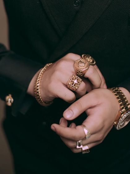 This close-up on the groom's hands adjusting his cuff showcases his collection of gold rings and luxury watch. It’s a detail shot that speaks to a modern, confident sense of style.