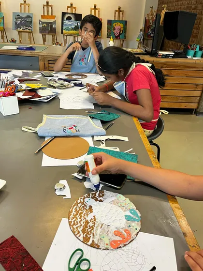 A busy table during a printmaking workshop, with students at different stages of creating their collagraph plates.