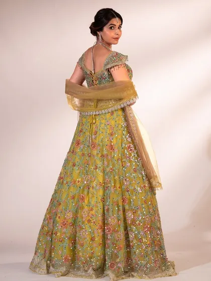 A back view of the green floral lehenga, showing the intricate tie-up detail of the blouse and the sheer dupatta.