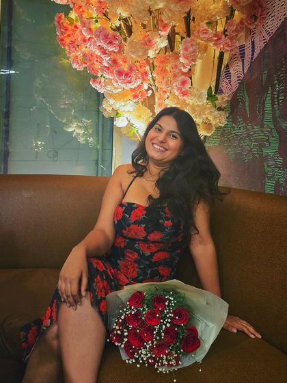 A smiling, confident portrait in this black and red floral dress. The setting, with the bouquet of roses, complements the romantic print of the dress, making it perfect for a birthday or anniversary celebration.