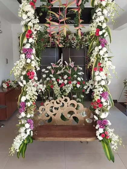 A beautiful wooden swing (jhula) decorated with elaborate floral arrangements for a housewarming celebration.