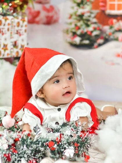 Get into the holiday spirit with a festive Christmas-themed photoshoot. This little one, dressed as Santa's helper, is surrounded by presents and snow, creating a magical holiday memory.