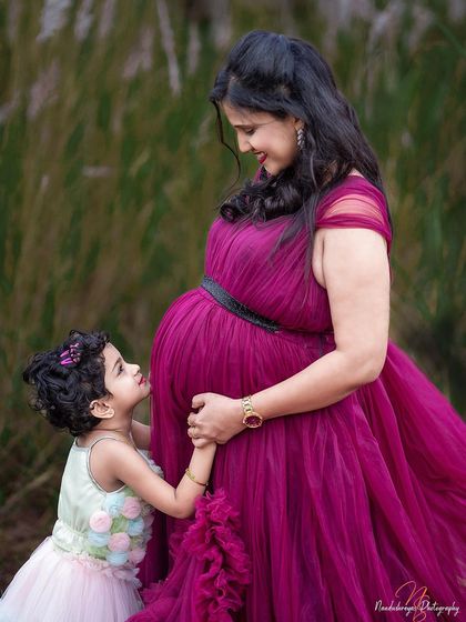 The connection between a mother and her daughter is so special. Here, a little girl looks up in awe at her mother's baby bump, a touching moment captured in a field of tall grass during this outdoor maternity session.