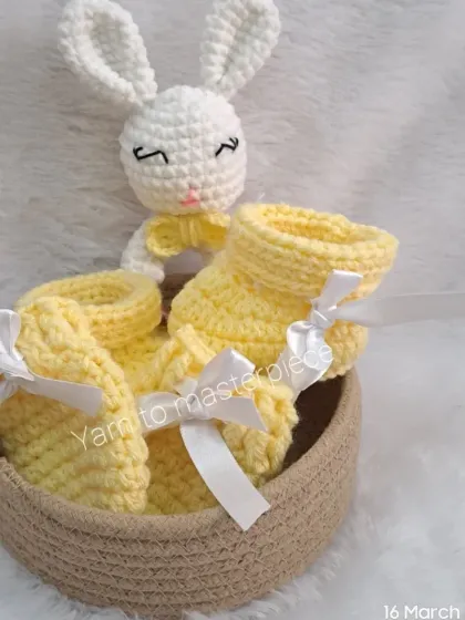 This newborn gift hamper in yellow and white is a complete set, including a bunny rattle, booties, and mittens, all tied with white satin ribbons.