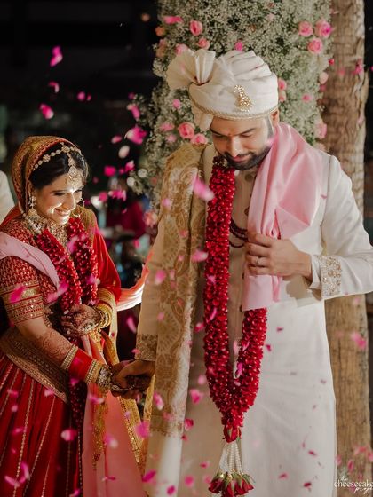 A candid shot of the couple holding hands, smiling at each other amidst a flurry of pink petals.