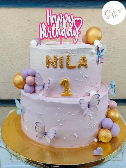 A beautiful two-tier butterfly cake for a first birthday. The pastel purple and pink ombre is decorated with delicate edible butterflies and clusters of matching baubles.