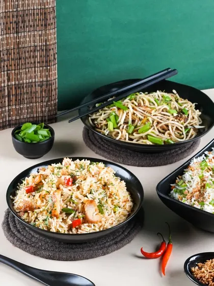 A spread of Indo-Chinese staples like Hakka noodles and fried rice. The dark bowls and minimalist styling on a two-toned background create a clean and contemporary look for a delivery menu.