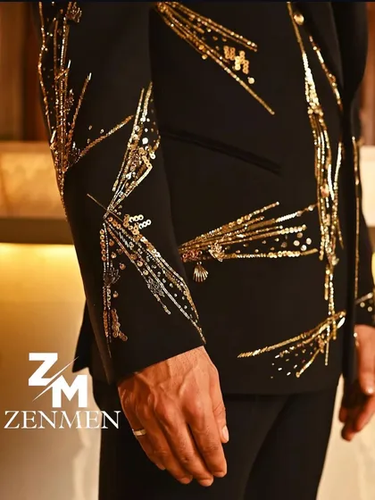 A close-up of the sleeve on the black and gold sequin tuxedo. The firework-like pattern is meticulously hand-embroidered, showcasing the detailed craftsmanship.