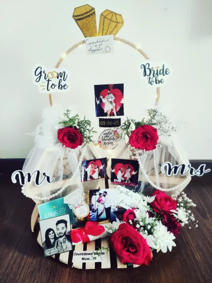 This engagement hamper is designed to celebrate a new beginning. It features a custom ring-shaped platter decorated with fresh flowers, personalized photos of the couple, and fun "Bride to be" and "Groom to be" signs, making it a perfect gift to mark the special occasion.