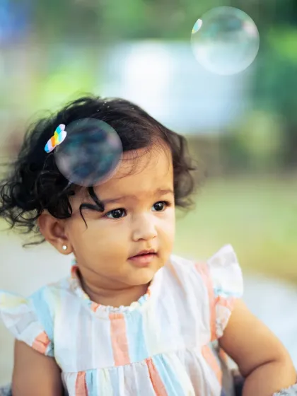 A whimsical outdoor portrait with a bubble floating right by her hair. These playful elements make photoshoots fun for kids and result in magical, candid images.