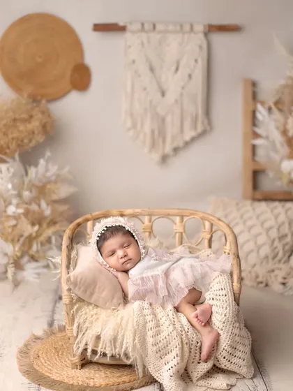 A full view of the dreamy, boho-inspired setup with a sleeping newborn in a rattan bed.