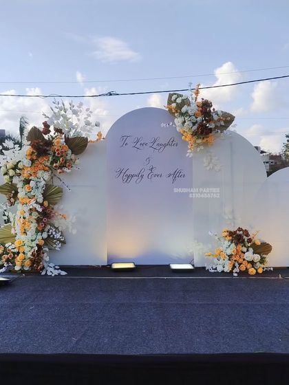 A modern and minimalist outdoor stage backdrop with white panels and artistic floral arrangements.