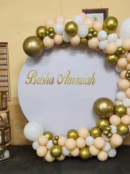 An elegant circular backdrop for a baby shower or naming ceremony. The white and gold balloon garland complements the gold "BABY" blocks on the side.