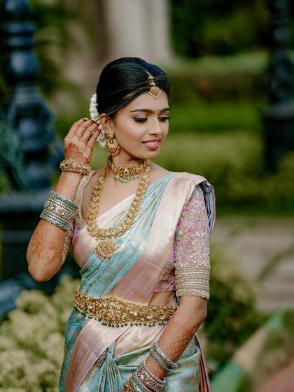 A close-up of the bride, showing the delicate embroidery on her pastel blouse and her traditional gold jewelry. The soft colors create a look of gentle elegance.