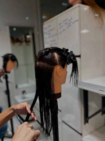 A close-up of a student practicing a precision haircut on a mannequin. We emphasize clean sectioning and steady-handed techniques as the foundation of a great cut.