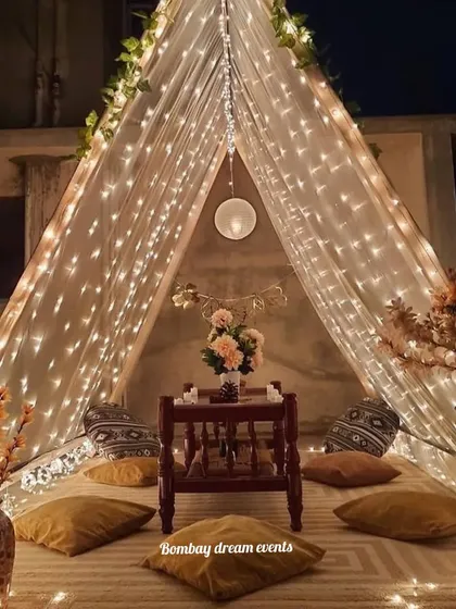A beautiful bohemian-style tent setup on a terrace. Illuminated by fairy lights and decorated with flowers and comfy cushions, it's the perfect spot for a proposal or an intimate dinner date.