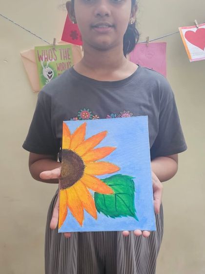 A student proudly holds up her completed acrylic painting of a sunflower. It's so rewarding to see them complete a project from start to finish.