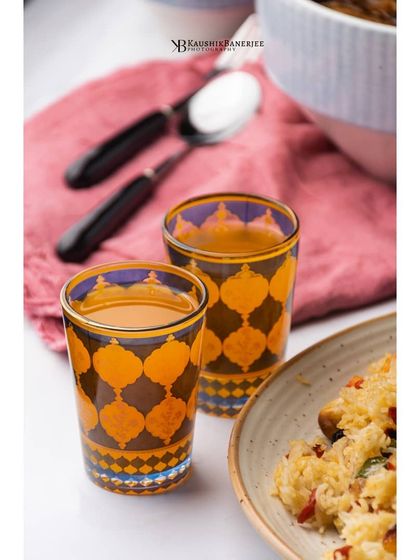 This shot captures a casual, sunny vibe with these patterned glasses filled with a summer cooler. The bright pink cloth and partial view of a food plate create a realistic lifestyle scene, showing the product in use.