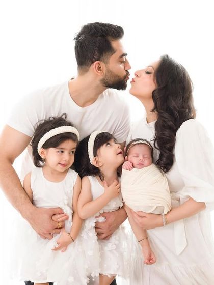 A portrait of a family overflowing with love. The parents and twin sisters all share a kiss in this heartwarming and beautifully chaotic moment.