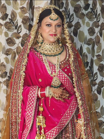 A beautiful bride in a pink and gold lehenga. The makeup features a soft, glossy finish with a defined eye, creating a look of pure elegance.
