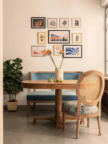 The dining nook is designed for both solo meals and intimate gatherings. A comfortable upholstered bench is paired with a classic cane-back chair, all centered around a gallery wall of art prints that reflect the client's personality.