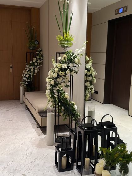 A modern entryway decorated with cascading white florals on a sleek black stand. The look is completed with black lanterns and candles, creating a sophisticated and welcoming first impression.
