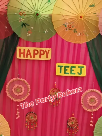 A vibrant and colorful photo booth backdrop for a Teej party. This setup features a pink drape background decorated with traditional Rajasthani umbrellas and handmade hangings.