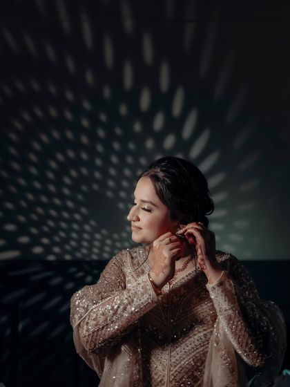 A beautiful solo portrait of the bride, Ravleen, as she adjusts her earring. The dramatic lighting creates a cinematic and introspective mood.