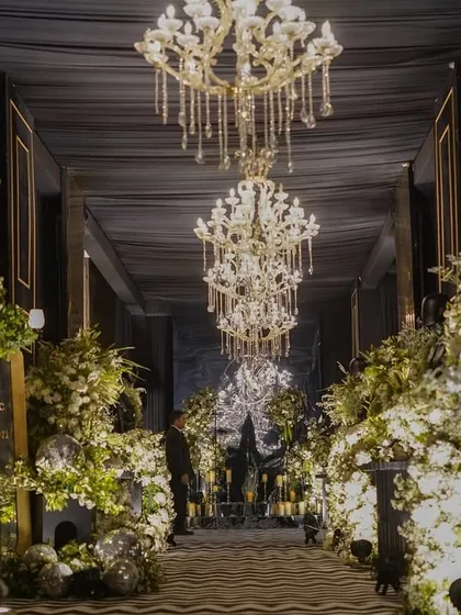For a modern Sangeet, we designed this dramatic black luxe entrance. The combination of deep, dark drapes, grand chandeliers, and abundant white florals creates a sophisticated and moody atmosphere, promising a night of glamour and high energy.