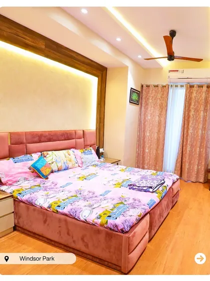 A cozy bedroom in Windsor Park with a pink upholstered bed and a wooden-paneled accent wall. The warm lighting creates a comfortable and inviting atmosphere.