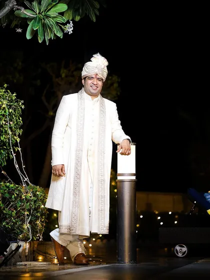 A handsome full-length portrait of the groom in his all-white sherwani, looking regal and ready for his wedding.