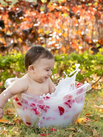 The perfect end to a fun day. A happy baby splashes in a milk bath with rose petals, set against a beautiful autumn-colored background.