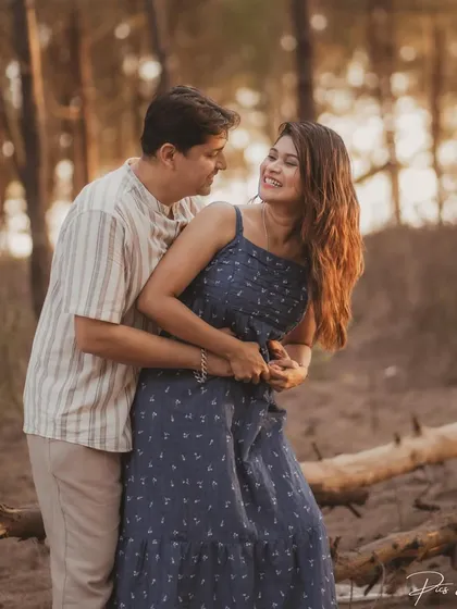 A happy, candid moment between a couple in a rustic, wooded setting. Their smiles and body language show their easy connection.