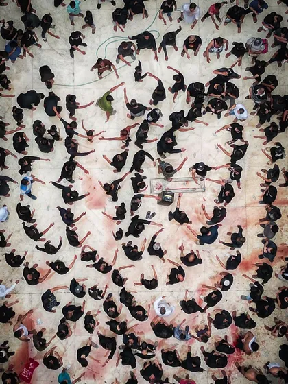 A closer top-down image of a Muharram ritual, focusing on the abstract patterns created by the participants. The stark contrast of black clothing against the ground creates a powerful and emotional visual story of faith and remembrance.