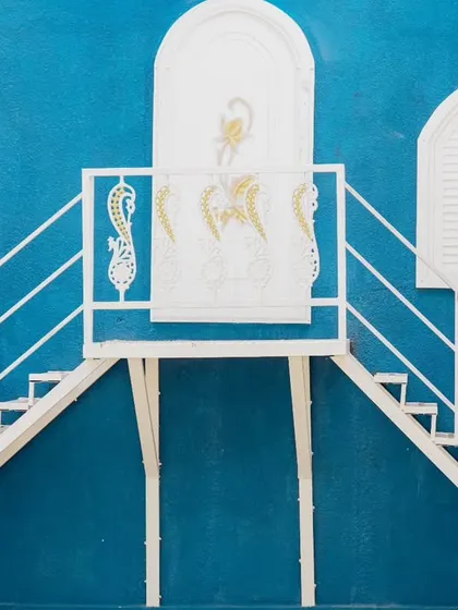 A wide, architectural shot of a couple on a unique staircase against a bright blue wall.