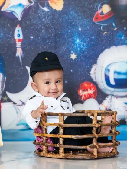 A six-month-old baby boy dressed as a pilot sits in a basket against a space-themed backdrop for his "halfway to one" shoot.
