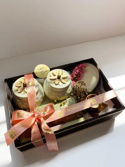 A sun-kissed shot of a sophisticated Diwali hamper. It features elegant ceramic jars and a decorative diya, all tied together with our custom branded ribbon.